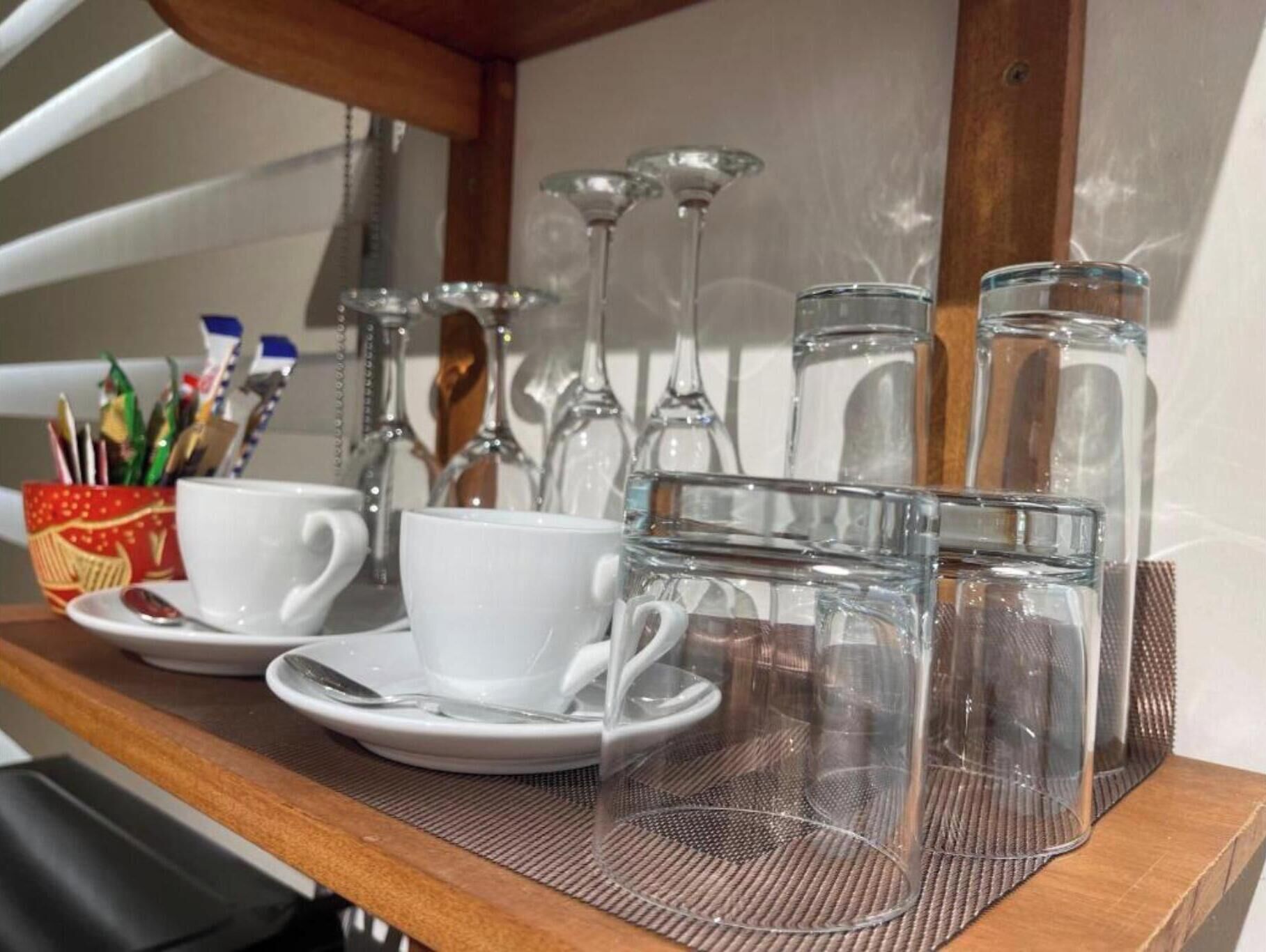 Una estantería de madera con tazas, platillos y botellas de vidrio transparentes, probablemente para agua u otras bebidas.