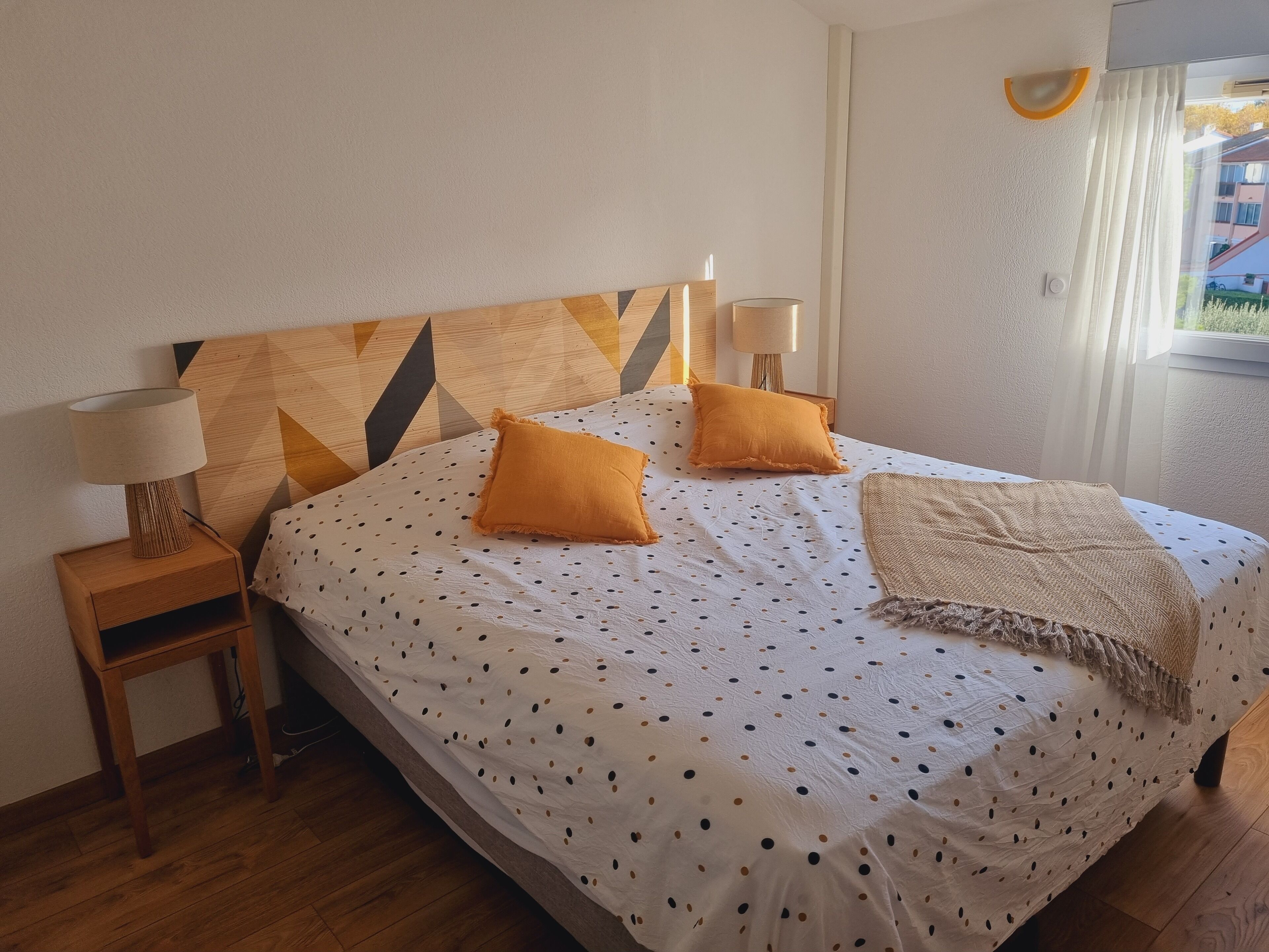 Un lit bien fait, avec une couvre-lit à pois, deux oreillers et un plaid.