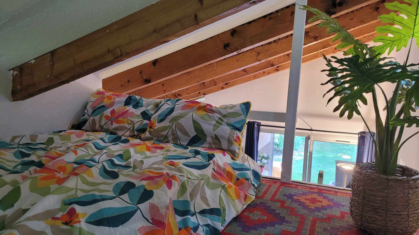 A bedroom with a bed, a potted plant, and a view of the outdoors.