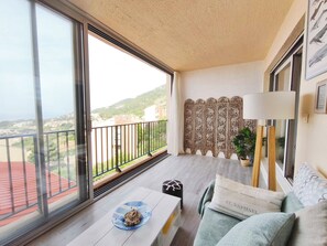En balkon med udsigt over et boligområde og bakker. Der er et bord med tallerken og en pude med tekst.