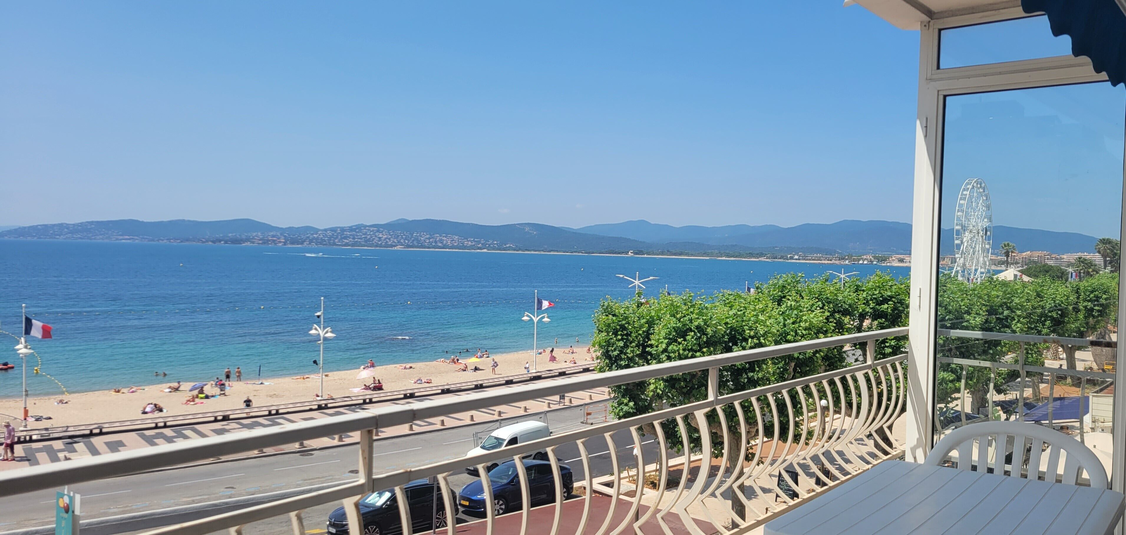 Un balcon avec vue sur une plage, une grande roue et des montagnes lointaines.