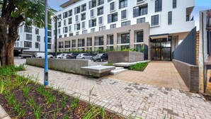 A modern hotel with a clean, white facade, a well-maintained outdoor area with a paved walkway, and a parking lot.