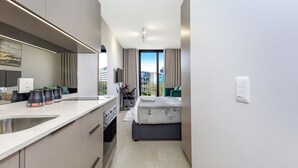 A modern hotel room with a kitchenette, a bed, a TV, and a view of the city.
