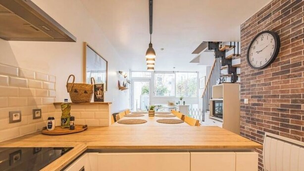 A modern kitchen with a wooden island, white cabinets, and a brick accent wall. - Urban loft with private garden - hyper center (REIMS)