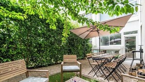 An outdoor patio with wooden furniture, a table with drinks, and a large umbrella. - Urban loft with private garden - hyper center (REIMS)