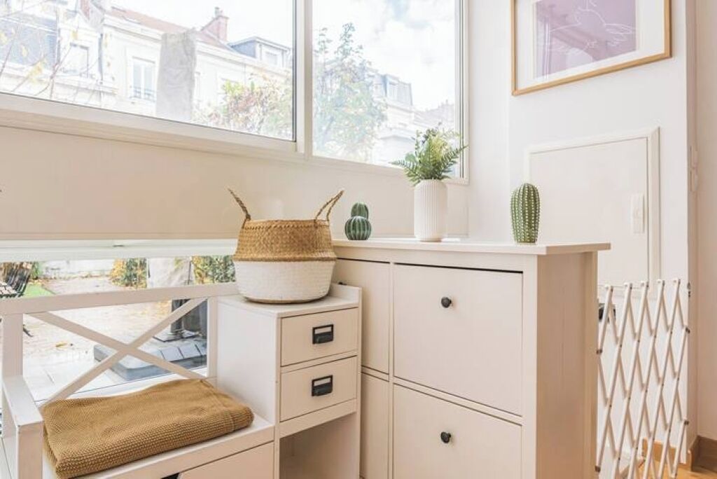 Une pièce lumineuse et bien éclairée, avec une fenêtre, un bureau blanc doté de tiroirs, un panier en osier et une plante succulente.