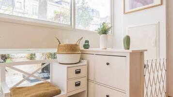 Une pièce lumineuse et bien éclairée, avec une fenêtre, un bureau blanc doté de tiroirs, un panier en osier et une plante succulente.