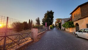 Une rue pavée, avec une zone délimitée par une clôture sur la gauche et un bâtiment sur la droite.