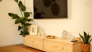 A wooden dresser with drawers, a large potted plant, a framed picture, and a small table with a bowl of fruit and a remote control. - NEW apartment costa da Caparica - 350 meters from the beach - boho style T2 (Costa da Caparica)