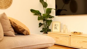 A modern living room with a sofa, a large plant, a flat-screen TV, and decorative woven items on the wall. - NEW apartment costa da Caparica - 350 meters from the beach - boho style T2 (Costa da Caparica)