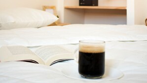 A bed with an open book and a glass of dark liquid, likely coffee, on a white bedspread. - NEW apartment costa da Caparica - 350 meters from the beach - boho style T2 (Costa da Caparica)