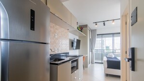 A modern kitchen with a stainless steel refrigerator, a built-in oven, and a microwave. There is a large window providing a view of the city. - Cozy Near Allianz Parque Sp-p1301b (São Paulo)