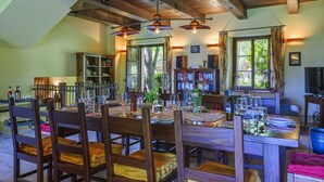 A dining area with a wooden table set for a meal, surrounded by chairs. There are bookshelves and a television in the background.