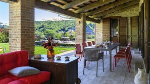 A covered outdoor dining area with a table set for two, red chairs, and a red sofa.