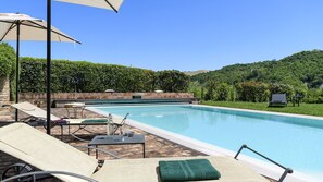 A swimming pool with lounge chairs and umbrellas, surrounded by greenery and stone walls.
