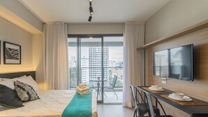 Hotellihuone, jossa on sänky, työpöytä ja kaksi tuolia, televisio sekä parveke, jolta on näkymä kaupunkiin.
