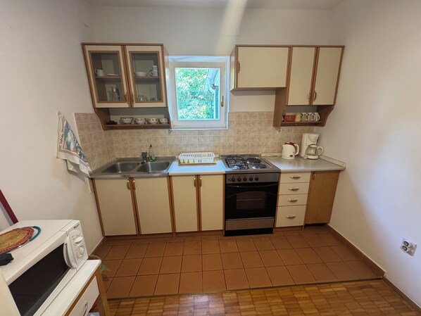 A compact kitchen with a gas stove, oven, and a window with a view of greenery. - Apartments Mila (Dramalj)