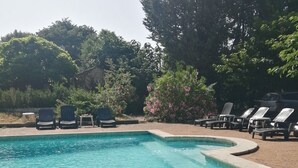 Una piscina rectangular con borde de piedras, rodeada de sillas de descanso y una pequeña mesa.