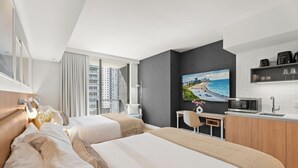 A hotel room with two beds, a desk, a microwave, and a large window with a city view.