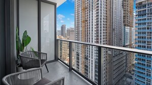 A balcony with a view of high-rise buildings, a potted plant, and two wicker chairs.