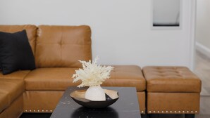 A brown leather sofa with a black cushion, a white vase with white branches, and a black table with a bowl. - Stylish4BR,5Bds,FREEPARKING,Near New York City, Times Square, WTC,BrooklynBridge (Bayonne)