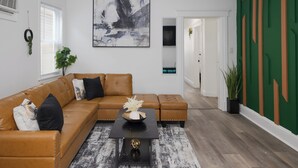 A modern living room with a brown leather sectional sofa, a black coffee table with a decorative bowl, and a large abstract painting on the wall. - Stylish4BR,5Bds,FREEPARKING,Near New York City, Times Square, WTC,BrooklynBridge (Bayonne)
