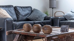 A modern living room with a black leather sofa, three wooden bowls on a wooden coffee table, and a floor lamp with a patterned shade. - Pipeland Farm Steading (No 4) (St Andrews)