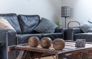 Ein modernes Wohnzimmer mit einem schwarzen Ledersofa, drei hölzernen Schalen auf einem Holztisch und einer Stehlampe mit einem gemusterten Lampenschirm.