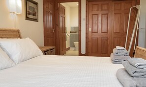 A bedroom with a bed, a nightstand, a mirror, and a stack of towels. - Pipeland Farm Steading (No 4) (St Andrews)