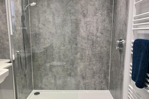 A shower with a glass door, a white sink, and a towel rack with a blue towel. - Pipeland Farm Steading (No 4) (St Andrews)
