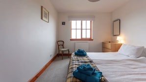 A bedroom with a bed, a chair, a nightstand, a lamp, and a window. - Pipeland Farm Steading (No 4) (St Andrews)