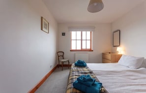 A bedroom with a bed, a chair, a nightstand, a lamp, and a window. - Pipeland Farm Steading (No 4) (St Andrews)