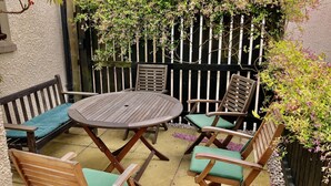 A patio with a round wooden table and six wooden chairs with green cushions. - Pipeland Farm Steading (No 4) (St Andrews)