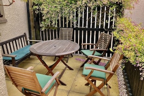 A patio with a round wooden table and six wooden chairs with green cushions. - Pipeland Farm Steading (No 4) (St Andrews)
