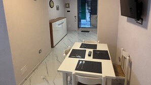 Een eethoek met een witte tafel en stoelen, een flatscreen televisie aan de muur en een klok.