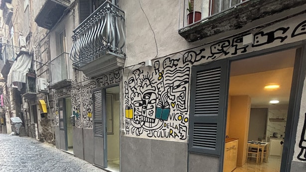 Een smalle straat met kinderaars, met een gebouw dat een metalen balkon en een deur met raam heeft.