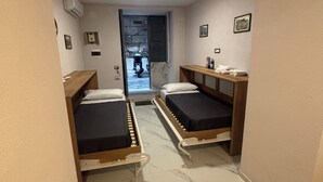 A hotel room with two single beds, a small table, a chair, a door leading outside, and a ceiling light. - House Of Fabio | A traditional townhouse in the historic center, surrounded by art and history (Napoli)
