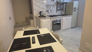 Een compacte keuken met een wit aanrecht, een gasfornuis, een koelkast en een marmeren achterwand.
