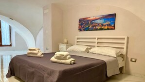 A hotel room with a large bed, a nightstand, a painting, and a window with curtains. - House Of Fabio | A traditional townhouse in the historic center, surrounded by art and history (Napoli)