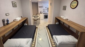 A room with two beds, a small table, and a kitchenette in the background. - House Of Fabio | A traditional townhouse in the historic center, surrounded by art and history (Napoli)