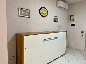 A room with a wooden cabinet, a white wall with framed pictures, and a tiled floor. - House Of Fabio | A traditional townhouse in the historic center, surrounded by art and history (Napoli)