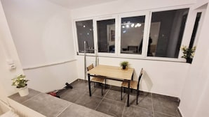 Un pequeño comedor con mesa y sillas de madera, una ventana con vistas, y una planta en maceta en el suelo.