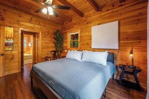 A wooden cabin bedroom with a bed, a ceiling fan, a nightstand, and a window. - 15+ Luxury log cabin w/ Hot Tub & Pool in Sevierville, minutes from Pigeon Forge (Sevierville)