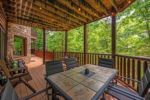 A covered outdoor deck with a stone wall, wooden railing, and a table with chairs. - 15+ Luxury log cabin w/ Hot Tub & Pool in Sevierville, minutes from Pigeon Forge (Sevierville)