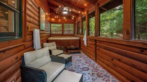 L’intérieur d’une cabane en rondins, doté d’un bain à remous, de meubles en osier et de grandes fenêtres offrant une vue sur la forêt.