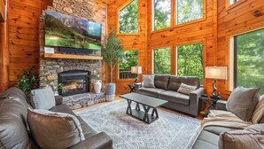 L’intérieur chaleureux d’un chalet en bois, avec une cheminée en pierre, des canapés en cuir et de grandes fenêtres donnant sur la forêt.