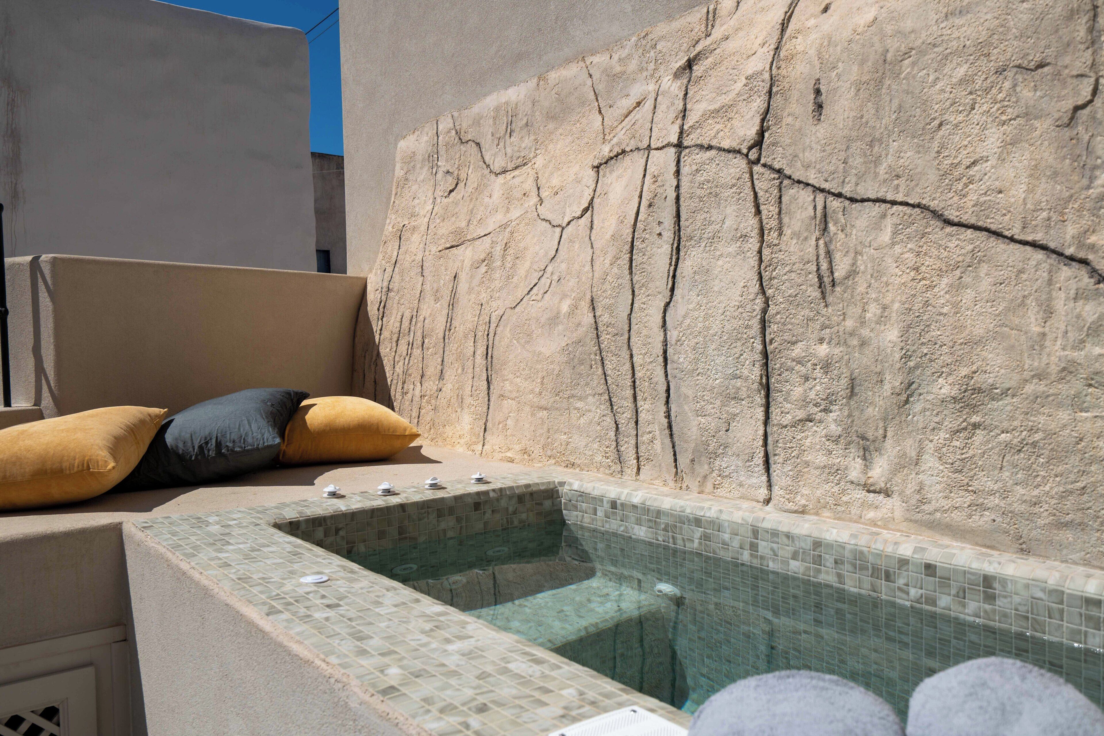 Ein Wellnessbereich mit einer Steinwand, einer gefliesten Hot Whirlpool und einer Sitzecke mit Kissen.