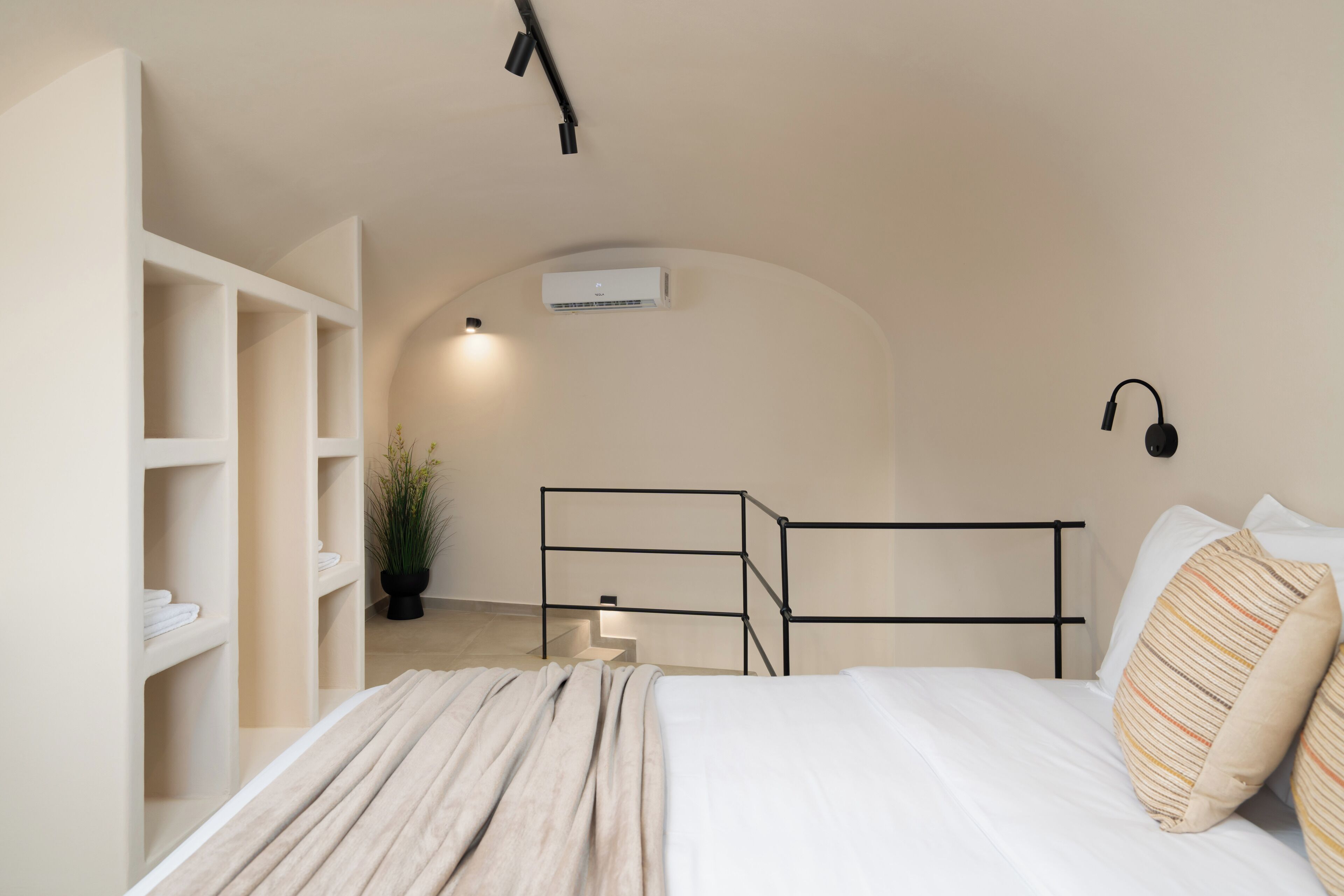 A bedroom with a bed, a bedside table, a wall-mounted air conditioner, and a potted plant.