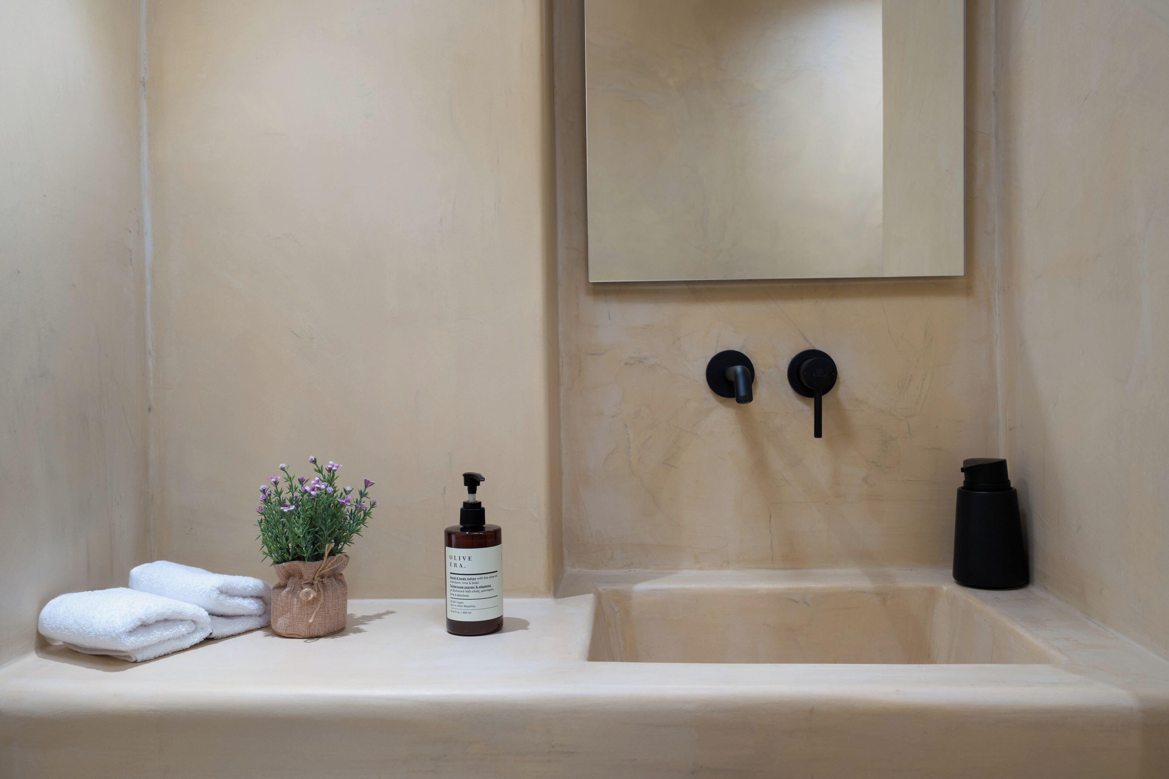 A bathroom with a sink, a mirror, a towel, a bottle, and a potted plant.