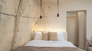 A bedroom with a large bed, a stone wall, and a hanging light fixture. - White Orchid Apartments (Santorini)